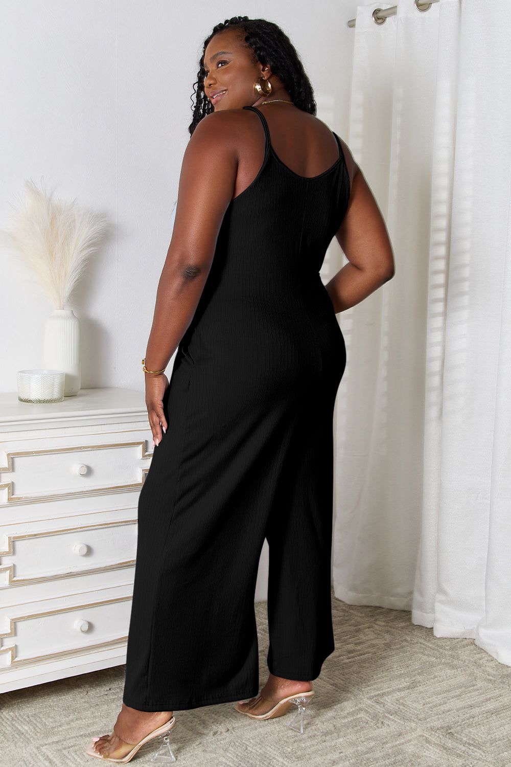 Black sleeveless wide-leg jumpsuit worn by a woman with curly hair.