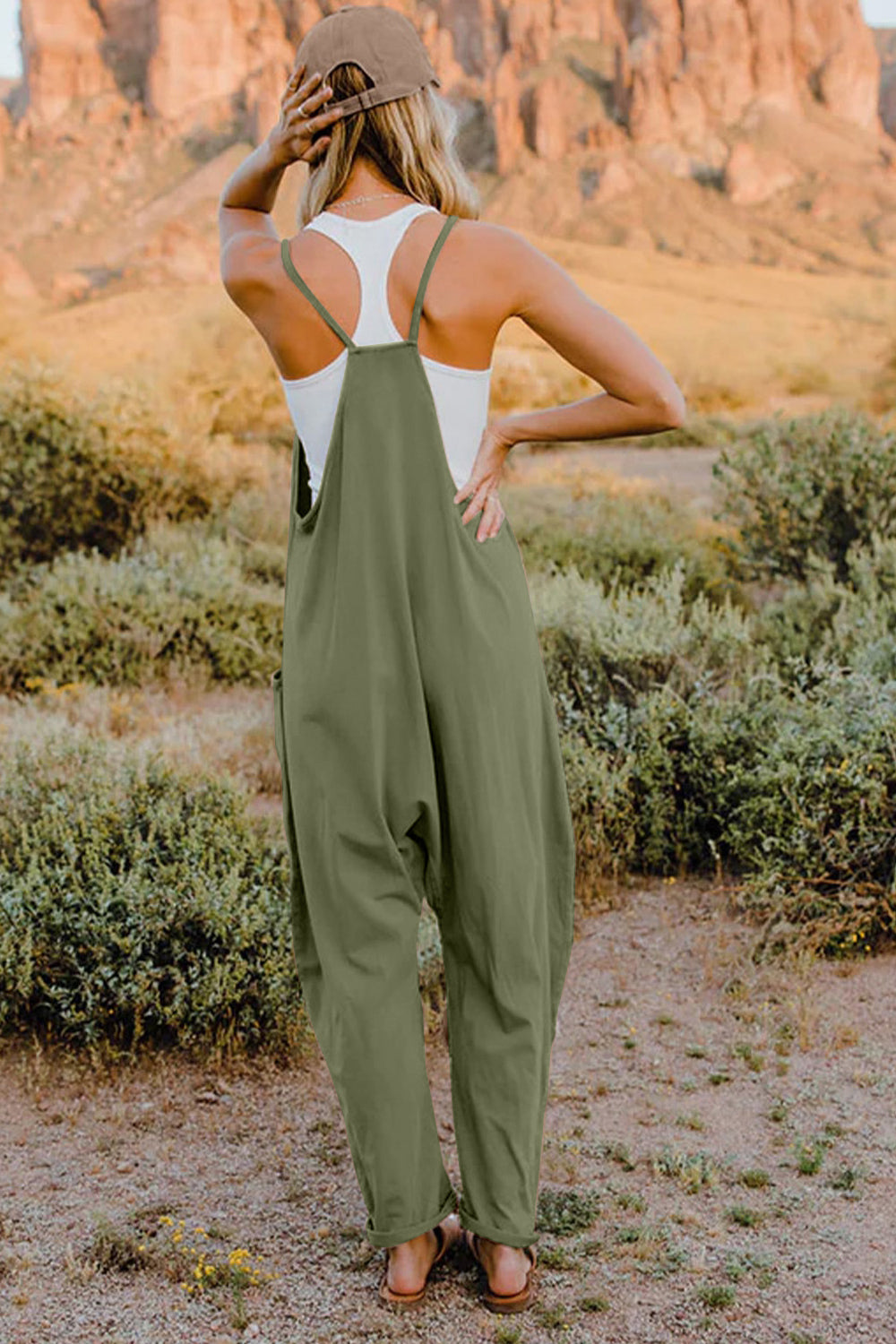 Woman wearing olive green overalls and a white tank top in a desert setting.