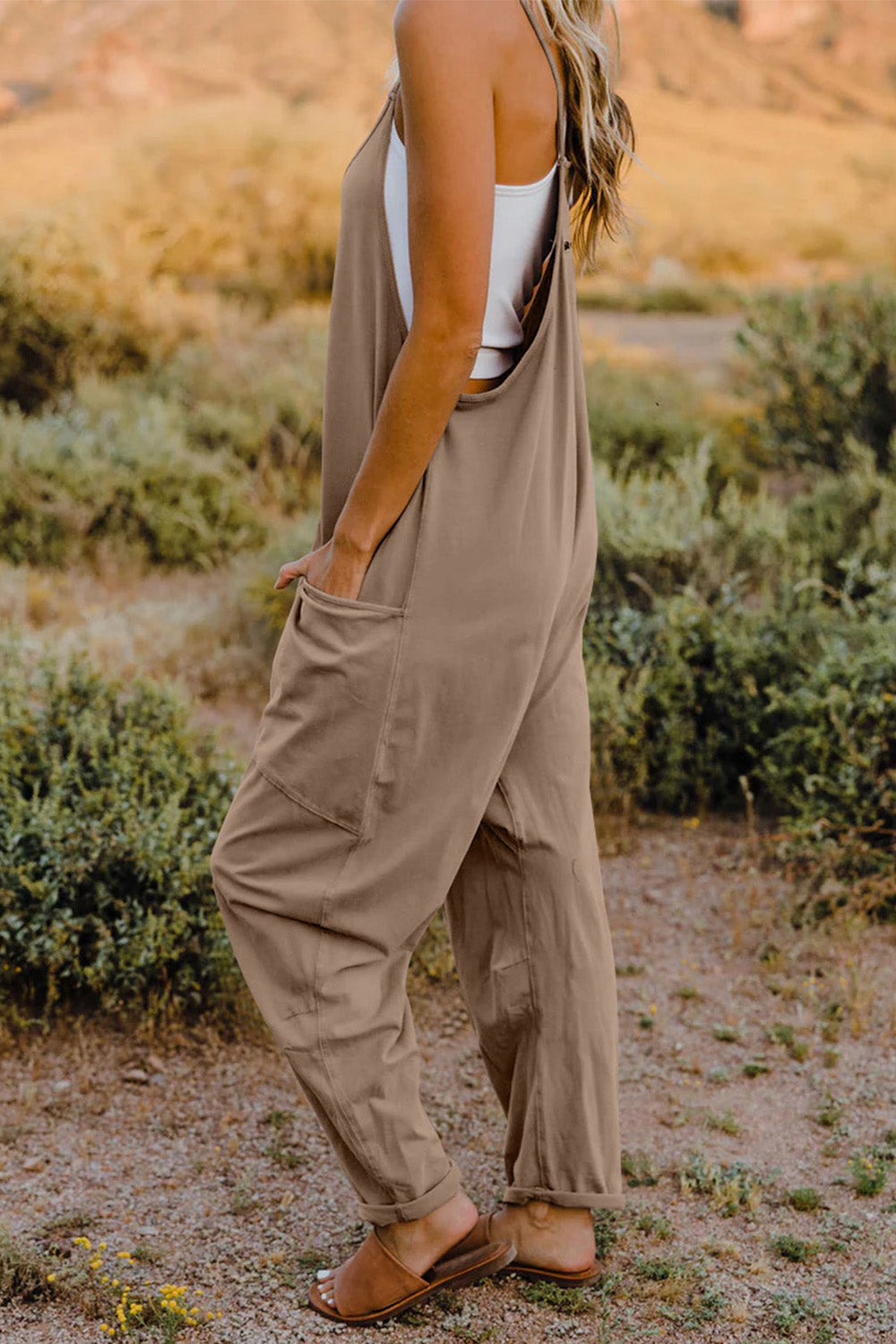 Loose-fitting beige jumpsuit with spaghetti straps and pockets.