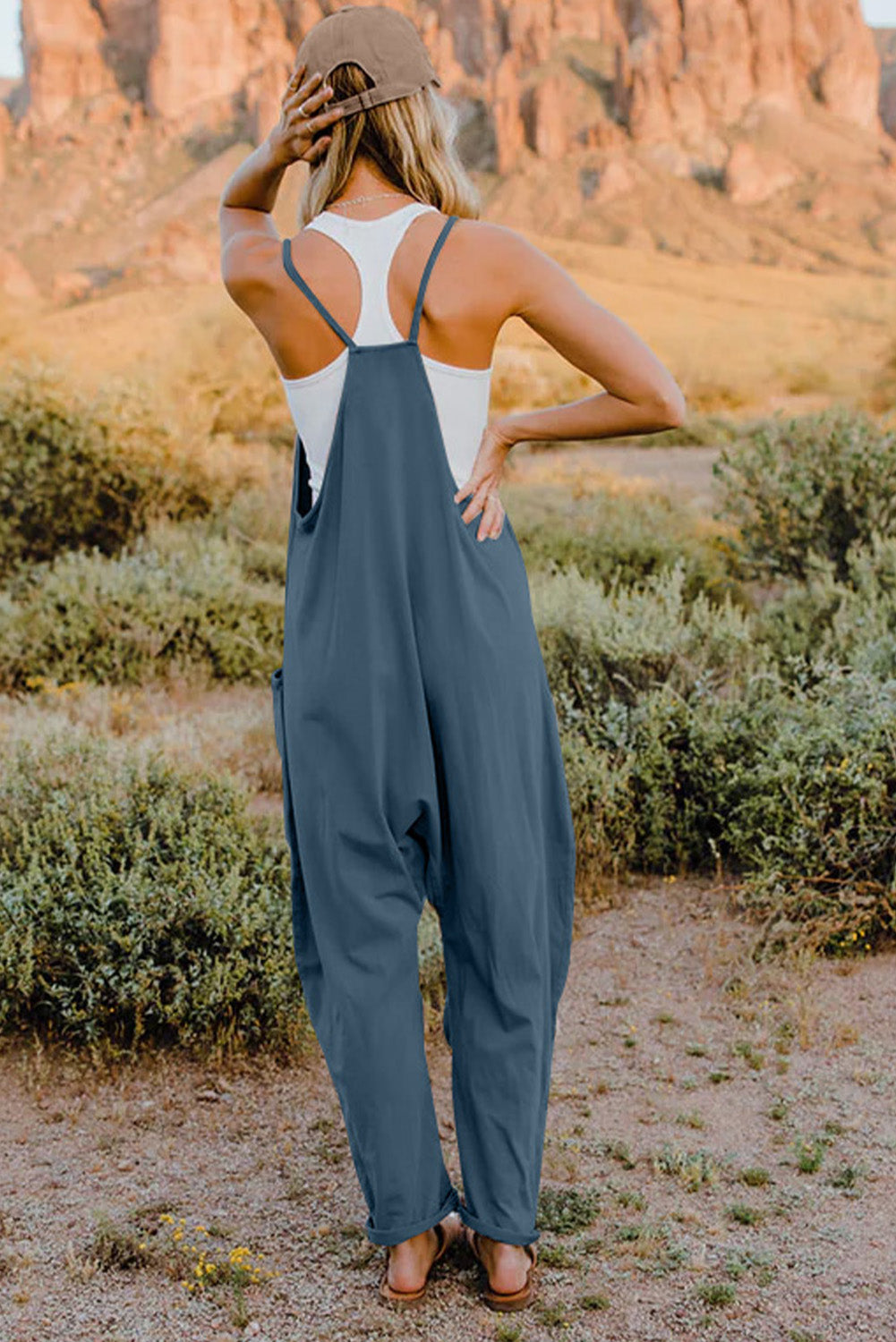 Woman wearing blue overalls and a white tank top in a desert landscape.