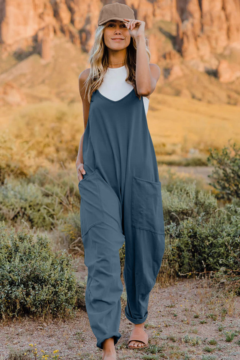 Blue denim overalls worn over a white top, paired with a beige cap.