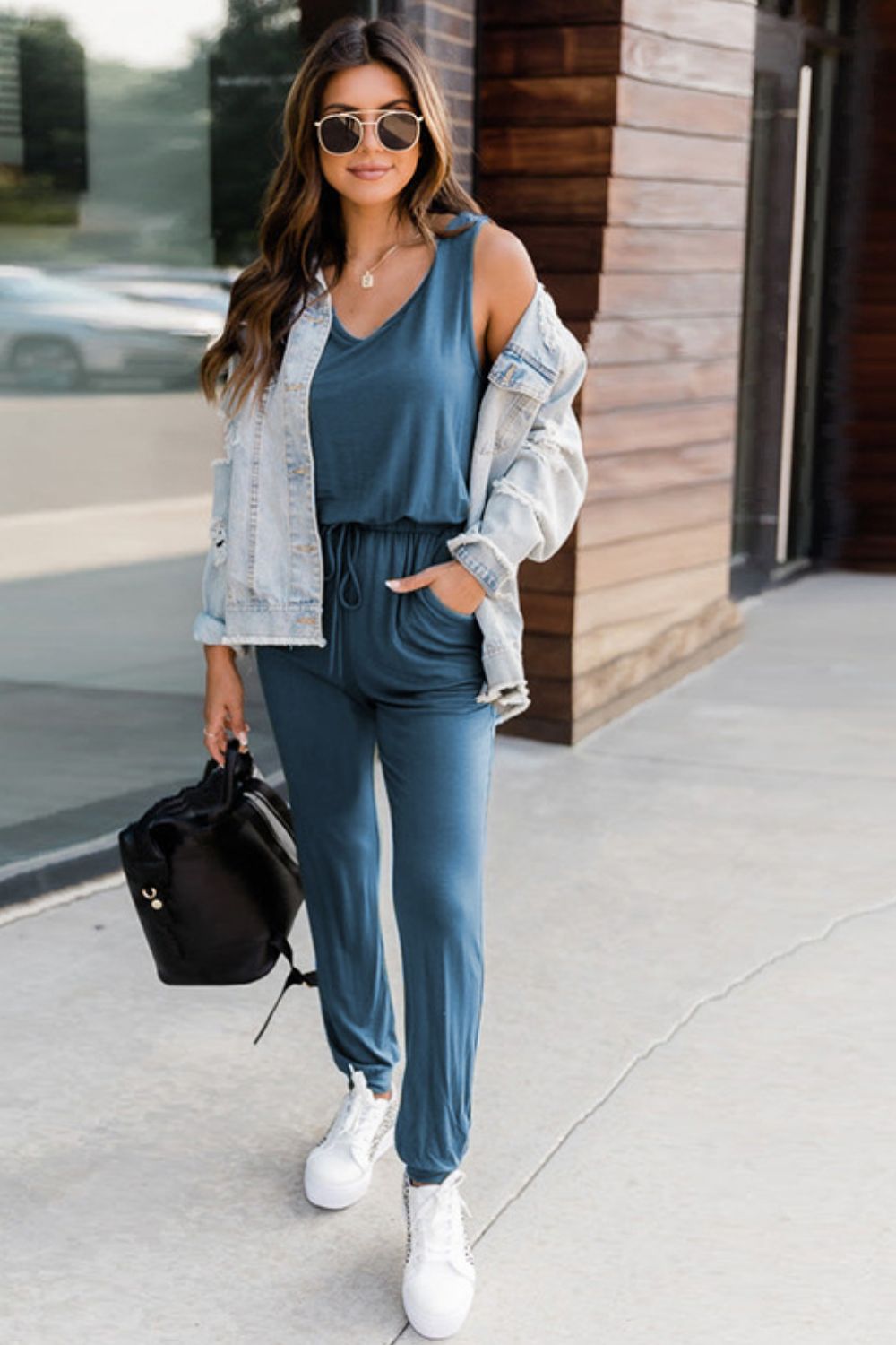 Woman wearing a casual blue outfit with sunglasses and a light jacket.